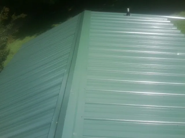 New green metal panels meeting at the ridge of a roof — Flat Roof Repair work by our crew in New London