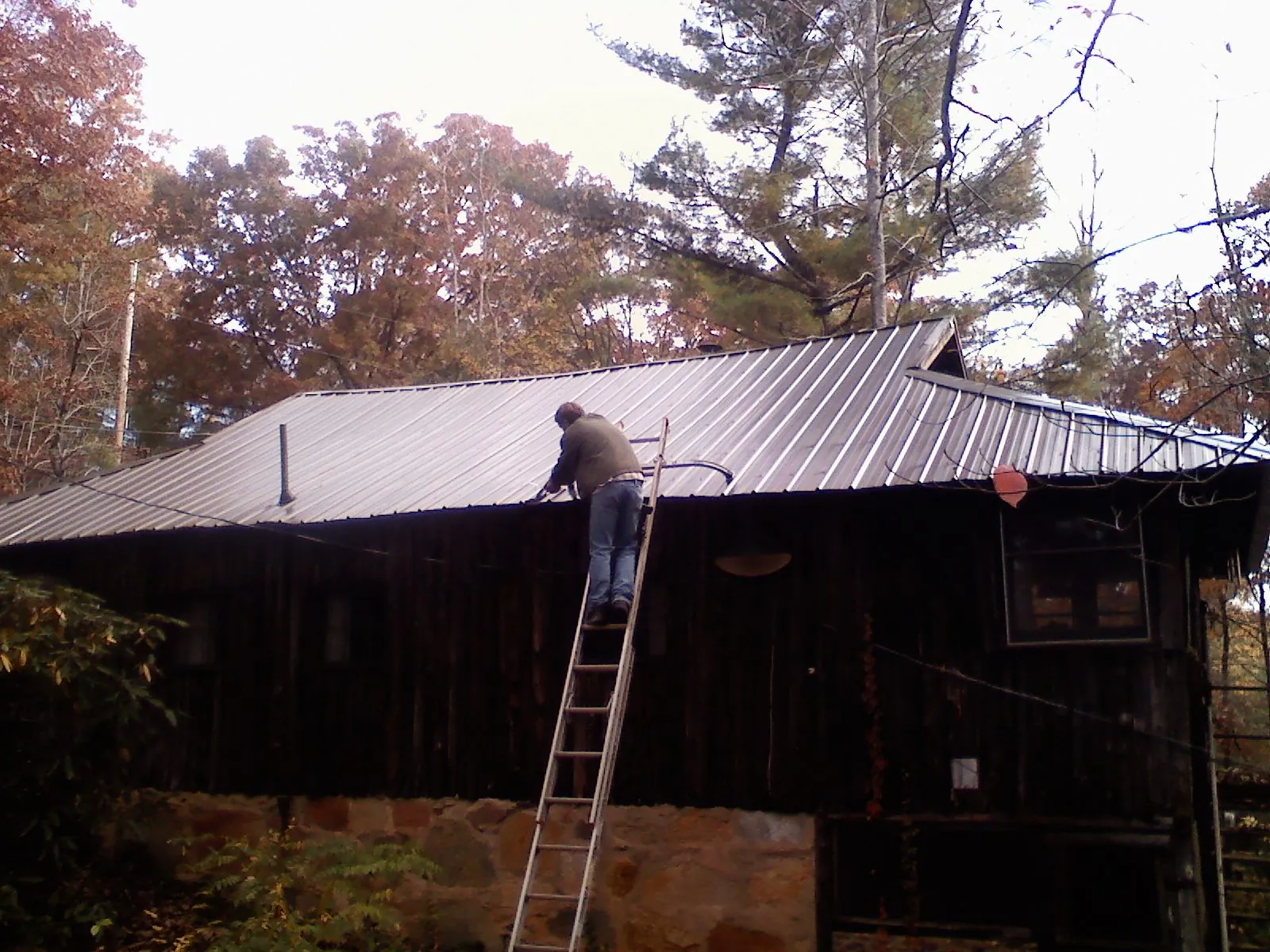 Roofer on a ladder working along the edge of a cabin metal roof in New London